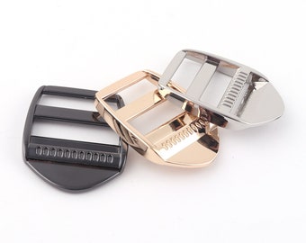 May include: Three metal slider buckles in black, gold, and silver. The buckles are designed to be used with webbing or straps.