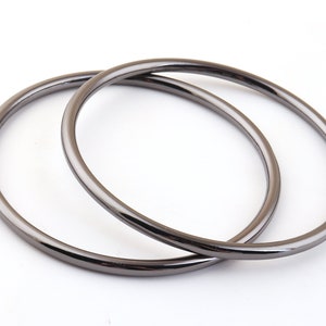 May include: Two black metal rings, one slightly larger than the other, are stacked on top of each other. The rings are smooth and have a shiny finish.