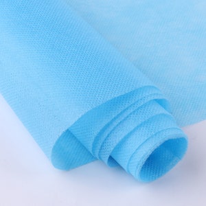 May include: A roll of light blue non-woven fabric. The fabric is rolled up tightly and has a smooth, even texture.
