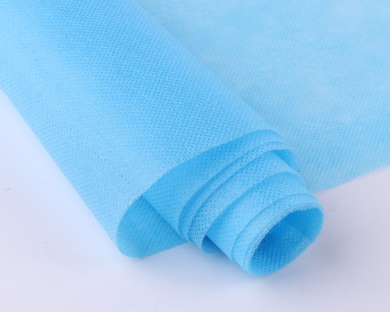 May include: A roll of light blue non-woven fabric. The fabric is rolled up tightly and has a smooth, even texture.