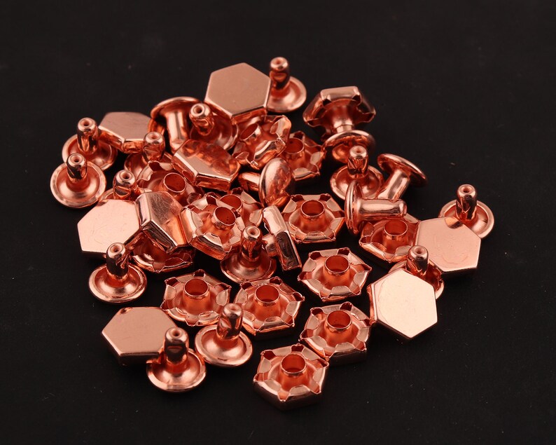 May include: A pile of copper-colored metal rivets with hexagonal heads and posts. The rivets are used for attaching fabric or leather together.