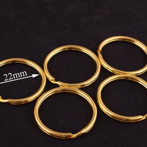 May include: Five gold-colored key rings, each with a diameter of 22mm. The key rings are arranged in a semi-circle on a black surface.