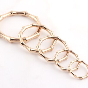 May include: A set of six gold-toned metal rings, each with a bamboo-like design. The rings are arranged in decreasing size, with the largest ring at the top and the smallest ring at the bottom.