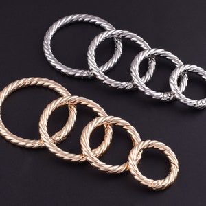 May include: A set of six silver and gold metal rings with a twisted rope design. The rings are of varying sizes and are arranged in a circle.