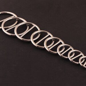 May include: A set of eight silver metal rings with a single bar across the center of each ring. The rings are arranged in order of size, with the largest ring at the top and the smallest ring at the bottom.