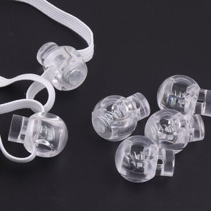 May include: Six clear plastic toggle clasps with a spring mechanism. The clasps are designed to be used with elastic cord or ribbon.