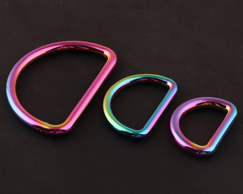 Może przedstawiać: Trzy tęczowe metalowe pierścienie w kształcie litery D w r&oacute;żnych rozmiarach. Pierścienie są w kolorze tęczy, w tym r&oacute;żowym, niebieskim, zielonym i fioletowym.