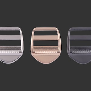 Puede incluir: Tres hebillas deslizantes de metal en plata, oro y negro. Cada hebilla tiene dos ranuras horizontales y un borde texturizado.
