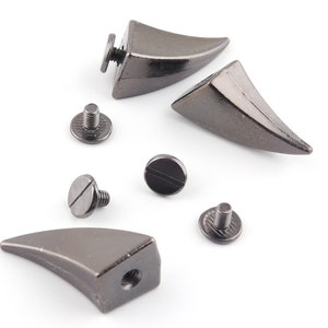 Puede incluir: Un conjunto de cuatro tachuelas de metal negro en forma de cuerno con tornillos. Las tachuelas son puntiagudas y tienen una forma ligeramente curvada. Son ideales para agregar un estilo punk rock o gótico a la ropa, las bolsas u otros accesorios.