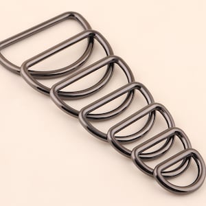 May include: A set of seven black metal D-rings of varying sizes. The rings are arranged in a graduated pattern, with the largest ring at the top and the smallest ring at the bottom.