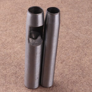 May include: Two silver metal leather hole punch tools. The tools are cylindrical with a round hole at the top and a smaller hole in the center of the cylinder.