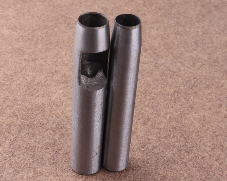 May include: Two silver metal leather hole punch tools. The tools are cylindrical with a round hole at the top and a smaller hole in the center of the cylinder.