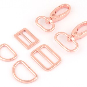 Peut inclure: Un ensemble de six pièces de quincaillerie en métal rose gold pour la création. L'ensemble comprend deux fermoirs pivotants, deux anneaux en D et deux boucles coulissantes.