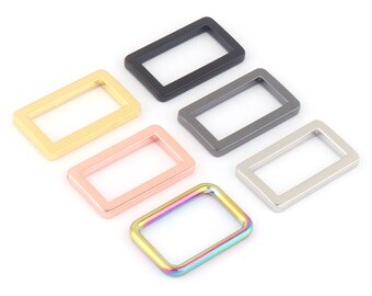 Könnte beinhalten: Sechs rechteckige Metallringe in verschiedenen Farben. Die Ringe sind in verschiedenen Schattierungen von Gold, Silber, Roségold, Schwarz und Regenbogen.