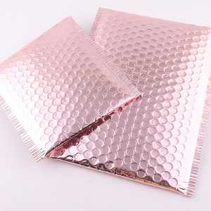 Pu&ograve; includere: Due buste a bolle metalliche rosa, anche note come buste imbottite, sono mostrate su una superficie bianca. Le buste sono realizzate in un materiale sottile e flessibile con uno strato di bolle d'aria per ammortizzare e proteggere.