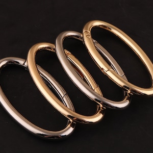 Puede incluir: Cuatro anillos metálicos ovalados, dos dorados y dos plateados, con un cierre de resorte. Los anillos están entrelazados, con los anillos dorados encima de los anillos plateados.