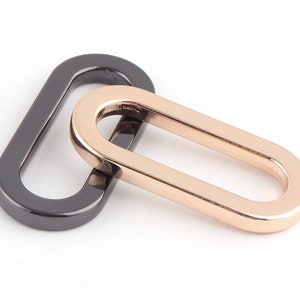 May include: Two oval-shaped metal rings, one black and one gold, linked together. The rings are smooth and have a polished finish.
