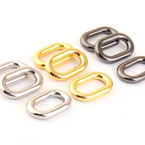 May include: A set of eight oval-shaped metal rings in silver, gold, and black finishes. The rings are all the same size and shape, but they have different finishes.