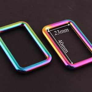 Może przedstawiać: Dwa metalowe pierścienie w kolorze tęczy, jeden o wymiarach 40 mm x 23 mm. Te pierścienie idealnie nadają się do dodania odrobiny koloru do Twoich prac ręcznych.