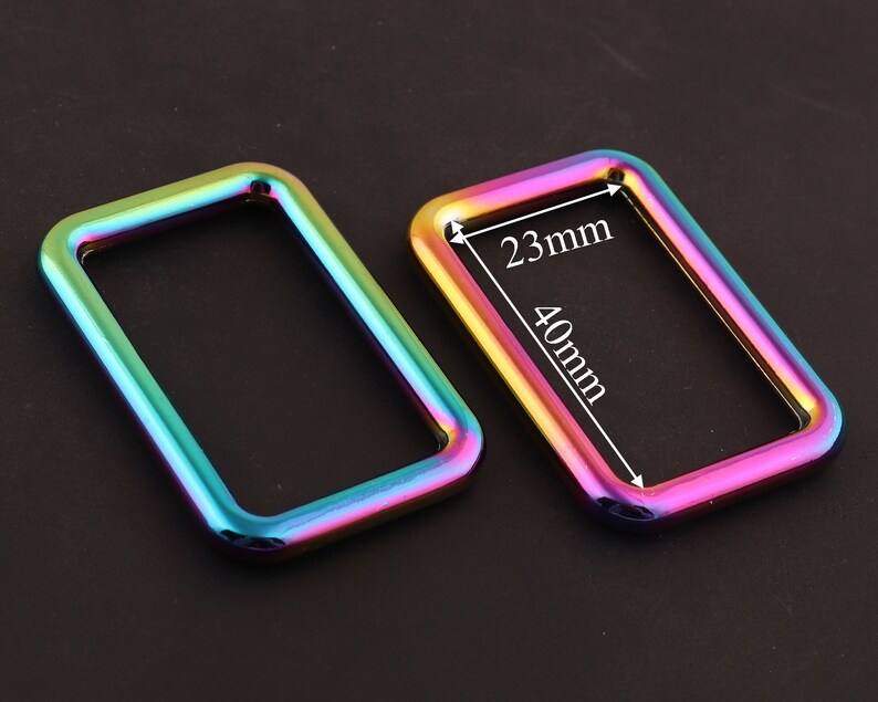 Może przedstawiać: Dwa metalowe pierścienie w kolorze tęczy, jeden o wymiarach 40 mm x 23 mm. Te pierścienie idealnie nadają się do dodania odrobiny koloru do Twoich prac ręcznych.