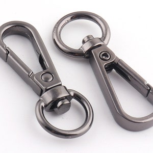 May include: Two black metal swivel clasps with a D-ring on one end. The clasps are commonly used for attaching keychains, bags, or other accessories.