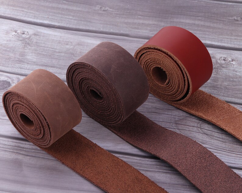 May include: Three leather straps rolled up, one brown, one dark brown, and one red. The straps are on a wooden surface.