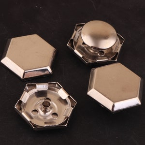 May include: Four silver-toned metal hexagonal-shaped decorative embellishments. Two of the embellishments have a raised center dome. The other two embellishments are flat.