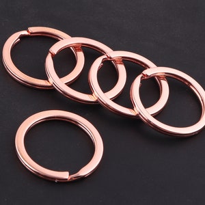 Peut inclure: Cinq anneaux de clés en or rose de différentes tailles, disposés en cercle sur une surface noire.