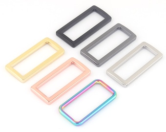 Könnte beinhalten: Fünf rechteckige Ringe aus Metall in verschiedenen Farben: Gold, Roségold, Silber, Schwarz und Regenbogen.