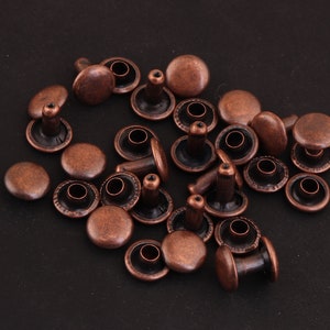 May include: A collection of copper-colored metal rivets with a raised center post. The rivets are arranged in a random pattern on a black surface.