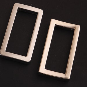 May include: Two silver metal rectangular frames with a smooth, polished finish. The frames are empty and have a slightly rounded edge.