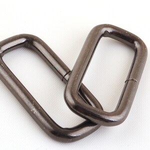 May include: Two black metal D-rings, each with a rectangular shape and a smooth, polished finish.