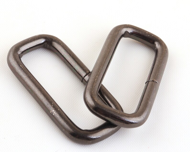 May include: Two black metal D-rings, each with a rectangular shape and a smooth, polished finish.