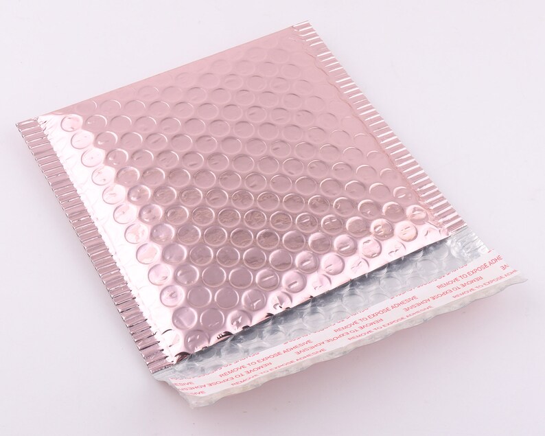 Pu&ograve; includere: Una busta a bolle metallizzata rosa con una striscia adesiva bianca che recita "REMOVE TO EXPOSE ADHESIVE".