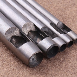 May include: Set of five silver metal hole punch tools with different sized circular openings. The tools are arranged in order of size, with the largest on the left and the smallest on the right.