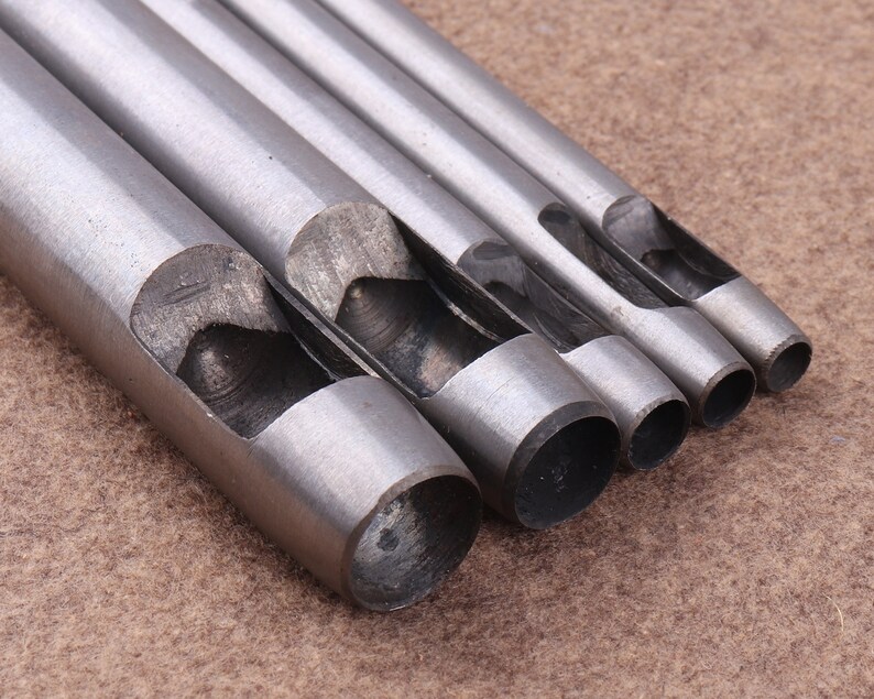 May include: Set of five silver metal hole punch tools with different sized circular openings. The tools are arranged in order of size, with the largest on the left and the smallest on the right.