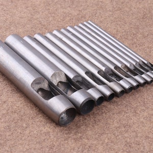 May include: A set of 12 metal hole punch tools, arranged in size order. The tools are silver in color and have a rounded edge.