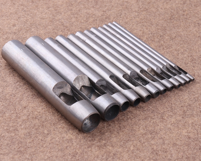May include: A set of 12 metal hole punch tools, arranged in size order. The tools are silver in color and have a rounded edge.