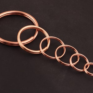 May include: A set of six gold-toned metal key rings of varying sizes. The key rings are arranged in a graduated size order, with the largest ring at the top and the smallest ring at the bottom.