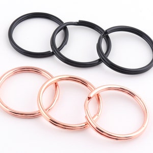 May include: Three key rings, two are rose gold and one is black. The key rings are linked together.