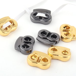 May include: Assortment of gold and black plastic toggle clasps. The clasps have two holes and are designed to be used with elastic cord or string.