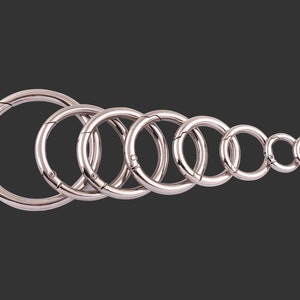May include: A set of eight silver metal key rings of varying sizes. The rings are all closed and are arranged in a row from largest to smallest.