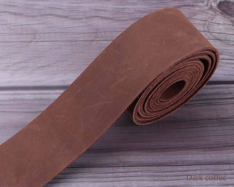 May include: A roll of dark brown leather strap, approximately 1 inch wide, on a wooden surface. The leather has a distressed, vintage look. "Dark coffee" is written in white text on the surface.