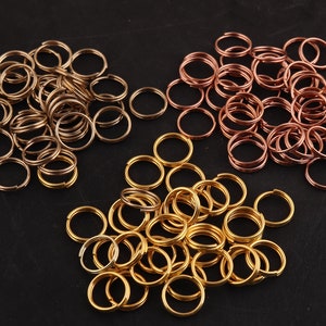 May include: A collection of gold, silver, and copper jump rings. The jump rings are arranged in three groups on a black surface.