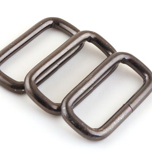 May include: Three silver metal D-rings, also known as belt loops, are arranged in a row. The rings are smooth and shiny, with a slightly rounded rectangular shape.