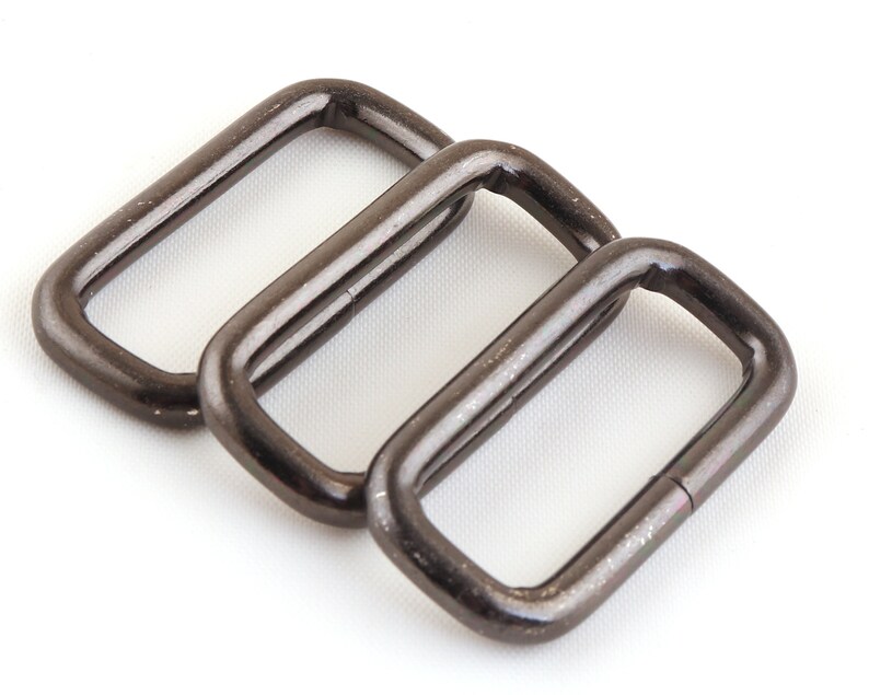 May include: Three silver metal D-rings, also known as belt loops, are arranged in a row. The rings are smooth and shiny, with a slightly rounded rectangular shape.
