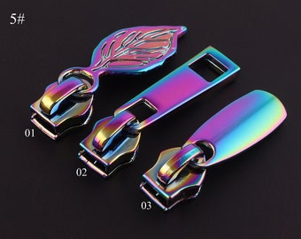 May include: Three iridescent zipper pulls with different designs. The first pull is a leaf shape, the second is a rectangular shape, and the third is a teardrop shape. The pulls are labeled 01, 02, and 03.