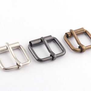 May include: Three metal belt buckles in different finishes: silver, black, and brass. Each buckle is a simple, rectangular design with a smooth finish.