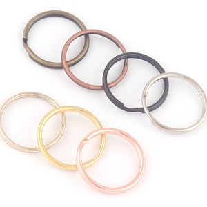 May include: A collection of metal split key rings in various colors, including bronze, copper, black, silver, gold, and rose gold. The rings are arranged on a white background, showcasing their circular shape and metallic sheen.