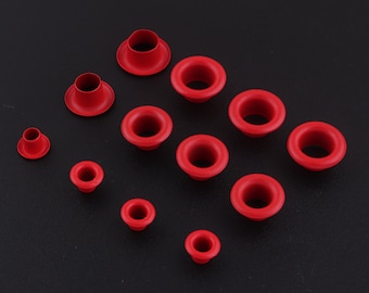 May include: Assortment of red metal eyelets in various sizes. The eyelets are arranged on a black surface.